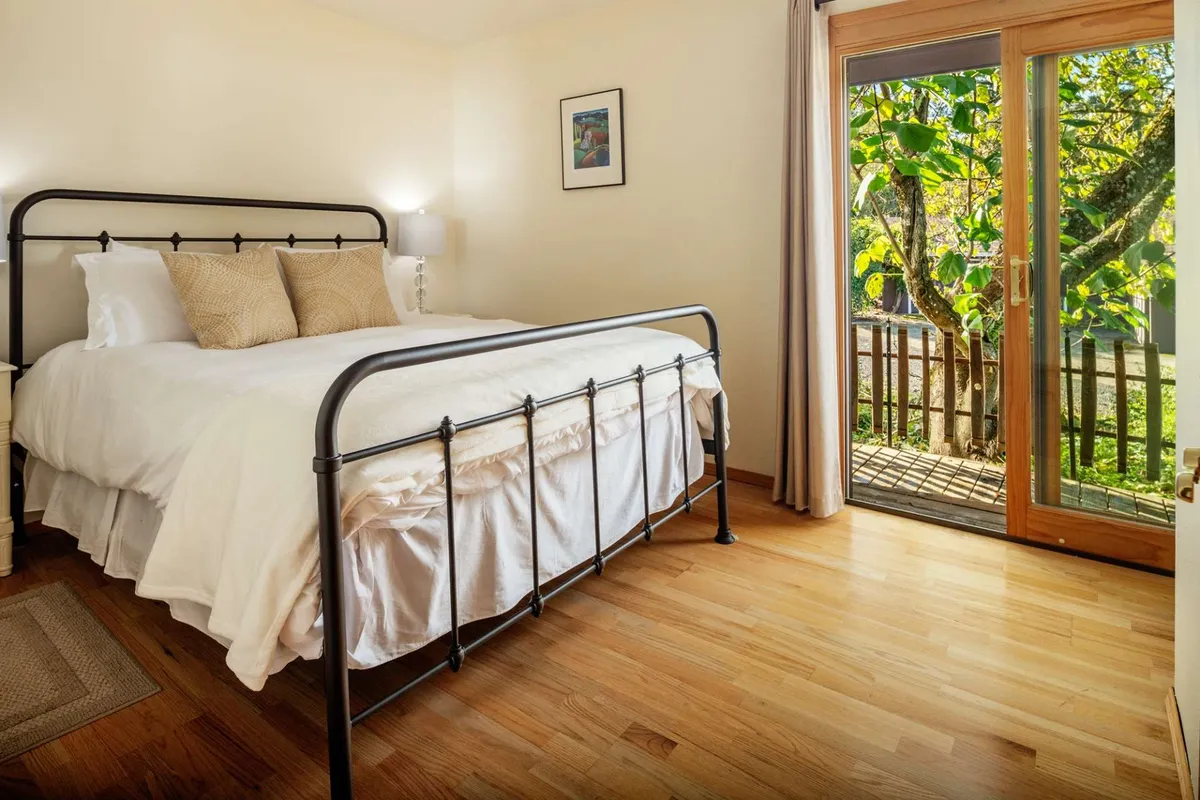 This shows a bedroom with a sliding glass door that opens to the outdoors, letting in abundant natural light. The bed and cozy decor highlight the comfort of waking up and stepping directly outside.