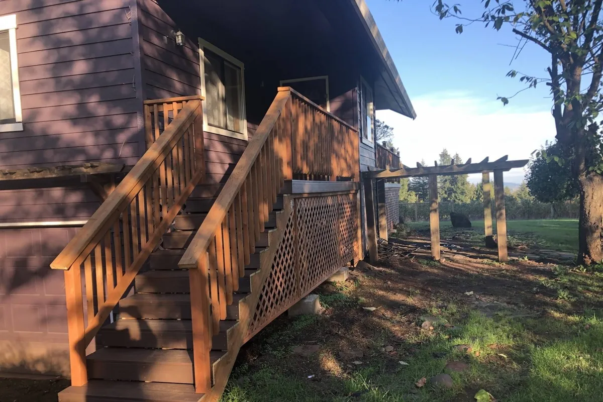 An inviting exterior scene featuring a staircase leading up to a spacious deck with a pergola, surrounded by greenery. This image hints at relaxing outdoor moments and the opportunity to enjoy vineyard or mountain views from the comfort of the property.
