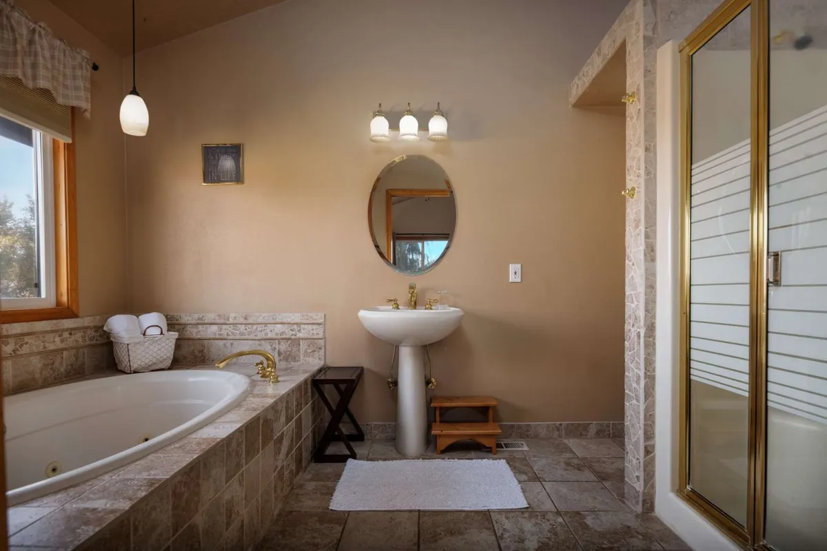 A modern bathroom interior featuring a spacious bathtub, sink, shower, and mirror. The space is light-filled and designed for comfort, creating a spa-like experience ideal for relaxation and self-care.