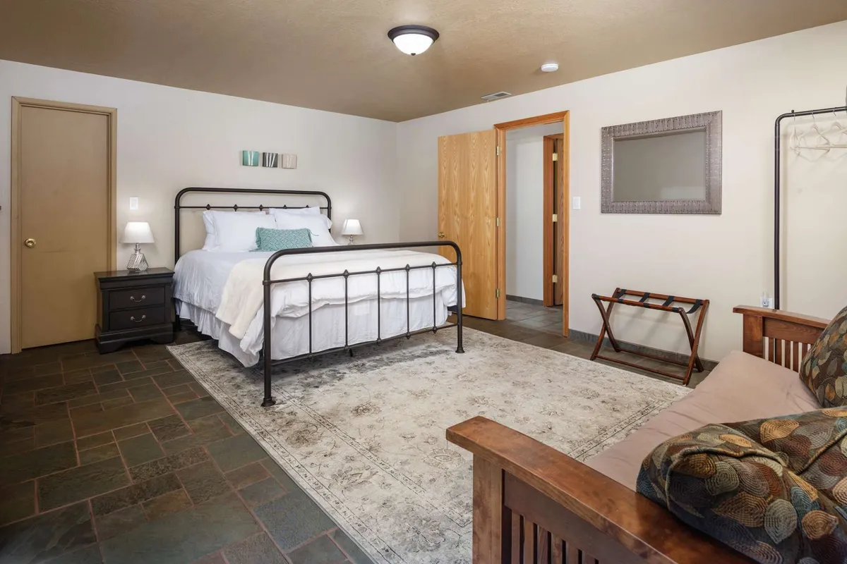 A bright, tranquil bedroom with a queen-sized bed dressed in crisp white linens, complemented by dark wood furniture and a soft area rug. The room is inviting, comfortable, and tastefully decorated, embodying the style and comfort mentioned for additional bedrooms.