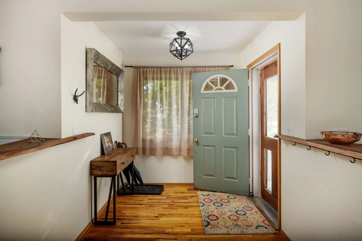 A welcoming entryway featuring a green front door, decorative mirror, wooden console table, and textured rug. The scene depicts first impressions as guests arrive, moments of reunion, and the transition from outside to the inviting interior of Pinot Vista, setting the tone for shared experiences.