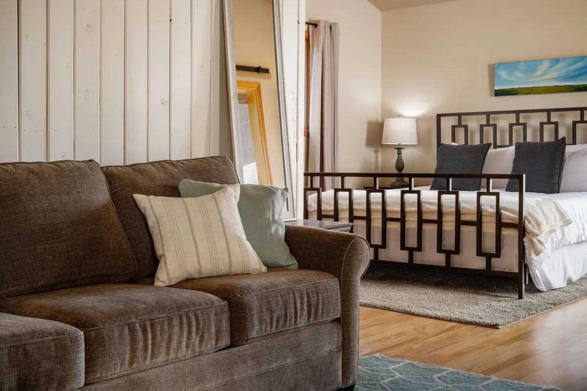 A cozy multi-use room with a comfortable sofa and a bed, decorated with a soft lamp and artwork. This flexible space can serve as an extra sleeping area, ideal for families or groups needing adaptable arrangements.